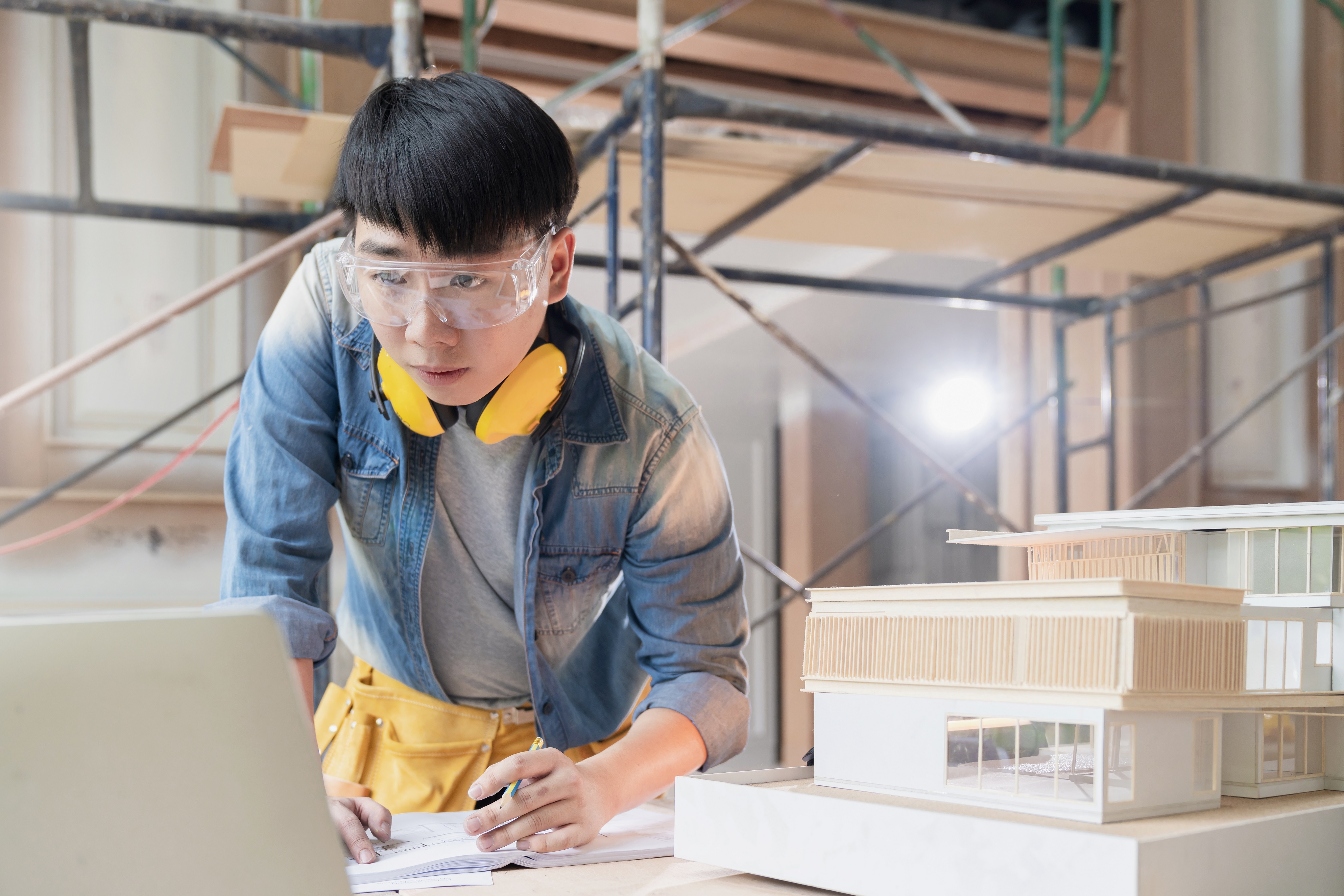 asian engineer male with uniform working with laptop and home mockup model analysis construction result with application technology at site construction home renovate and improvment background
